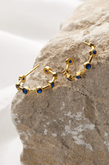 A beautiful pair of Handcrafted Seven Stone Hoop Earrings adorned with vibrant blue sapphires. These elegant earrings are made from 21ct gold-plated brass and are a stunning addition to any jewellery collection.