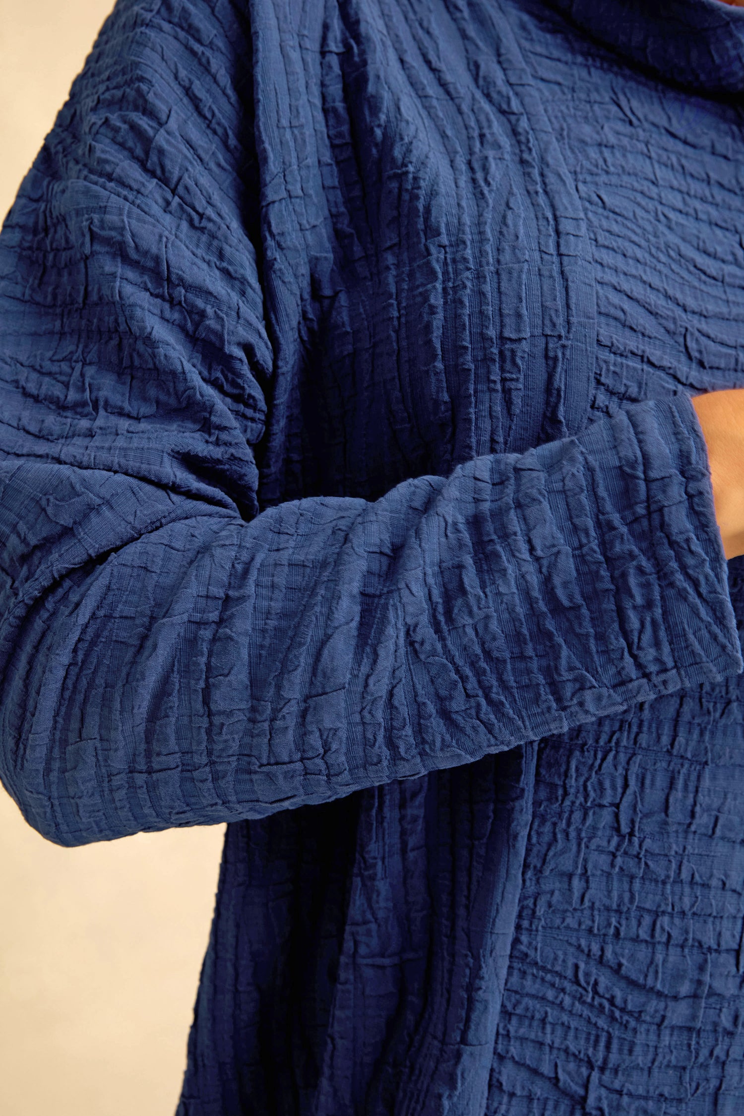 Close-up of a person’s arm and torso wearing the Wave Textured Crinkle Dress in blue, featuring a subtle bubble silhouette and textured long sleeves.