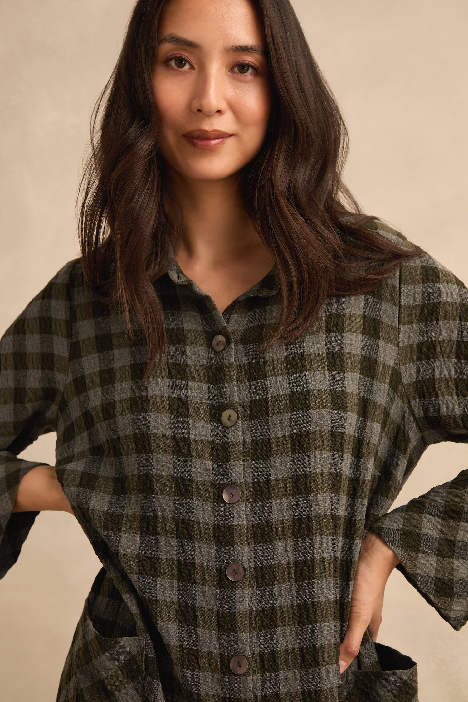 A woman with long dark hair stands against a neutral background, wearing the Crinkle Check Flared Jumpsuit and posing with her hands on her hips.