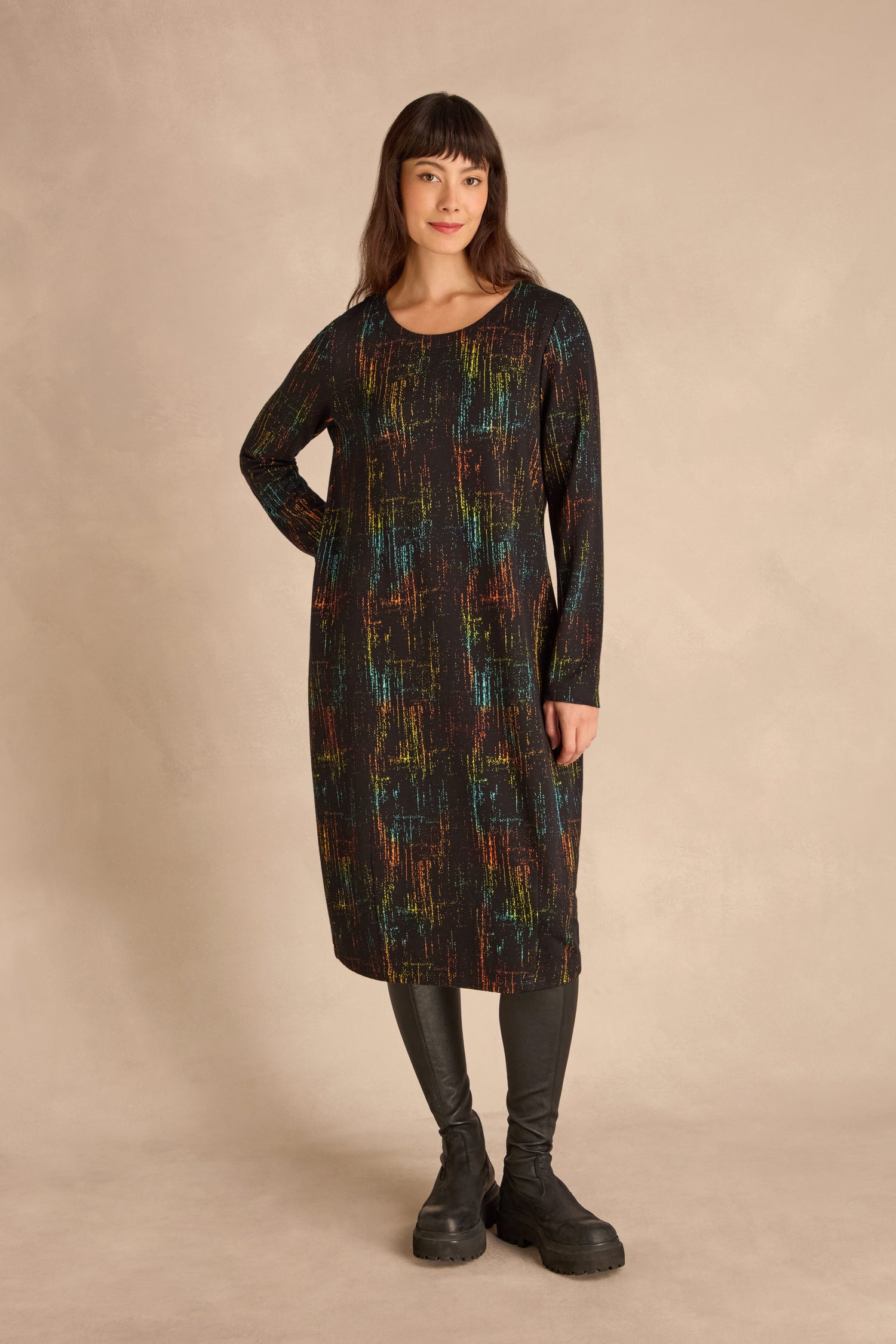 Woman standing in a studio wearing the Space Dye Jacquard Jersey Dress with black leggings and chunky black boots.