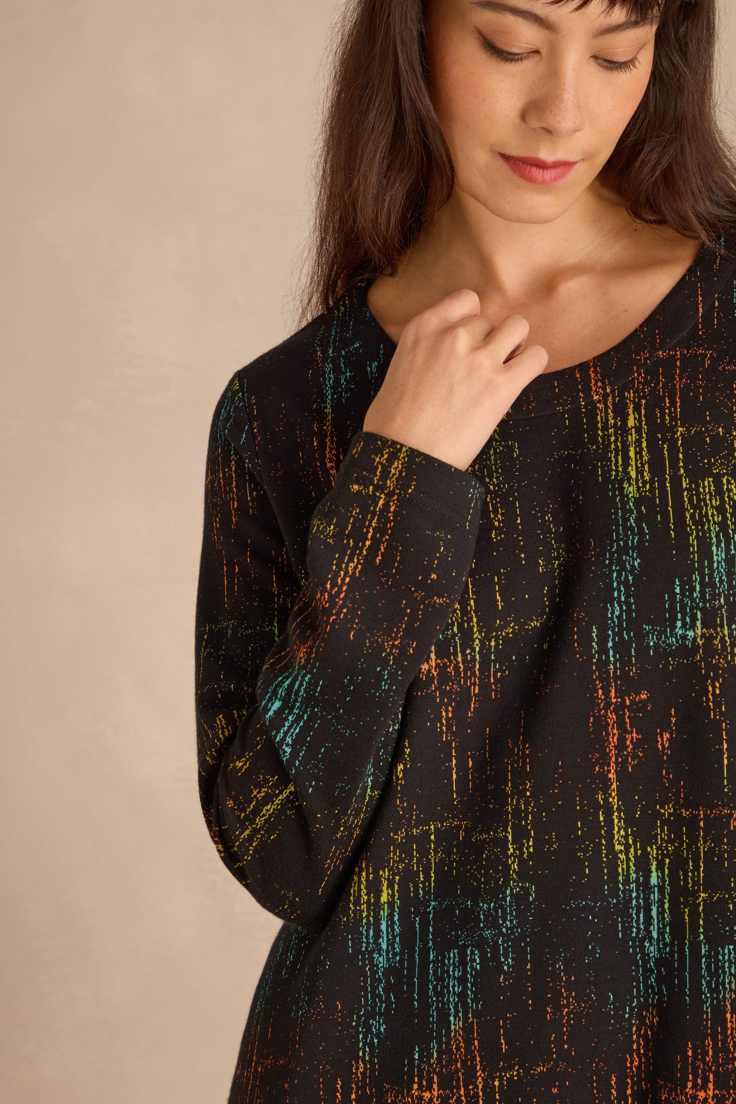A woman in the Space Dye Jacquard Jersey Dress stands against a beige background, touching her collar with her right hand and looking down.