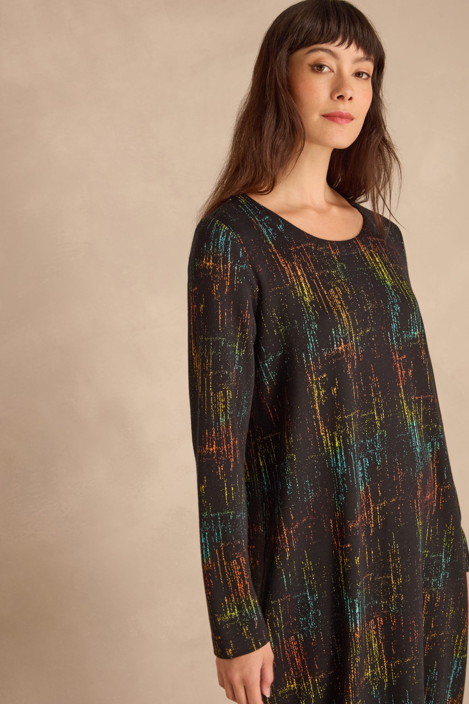 Woman wearing the Space Dye Jacquard Jersey Dress, featuring long sleeves and colorful abstract lines, stands against a neutral background.