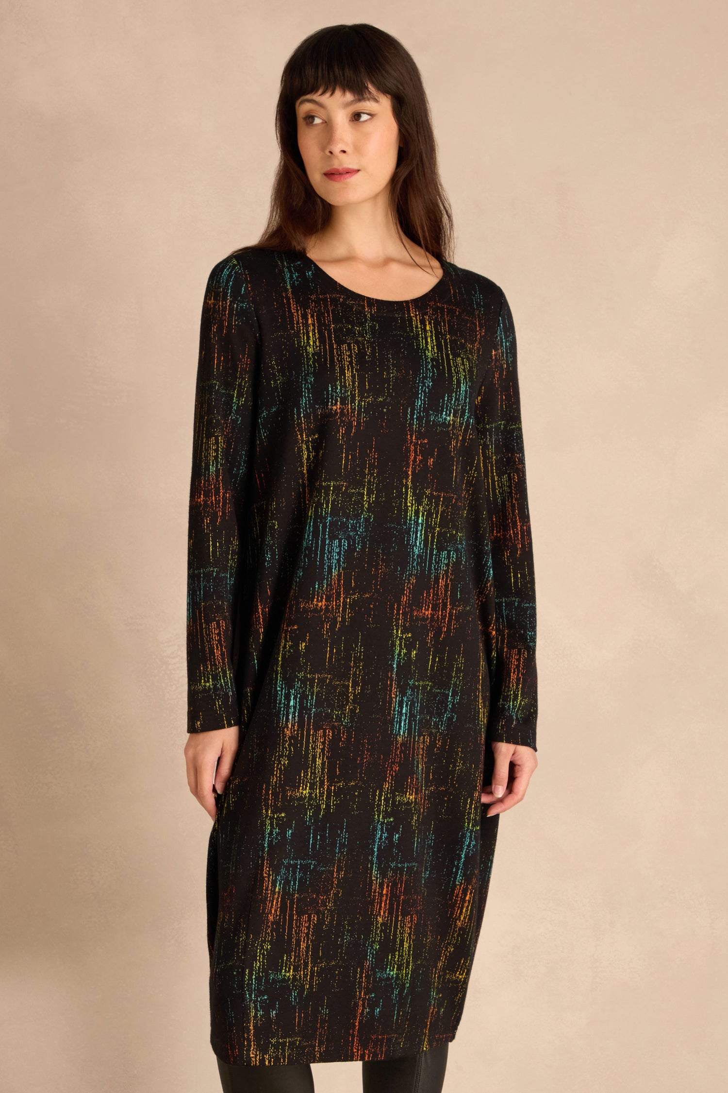 Woman in a Space Dye Jacquard Jersey Dress—long-sleeve, knee-length, black with a multicolored abstract pattern—standing against a light beige background.