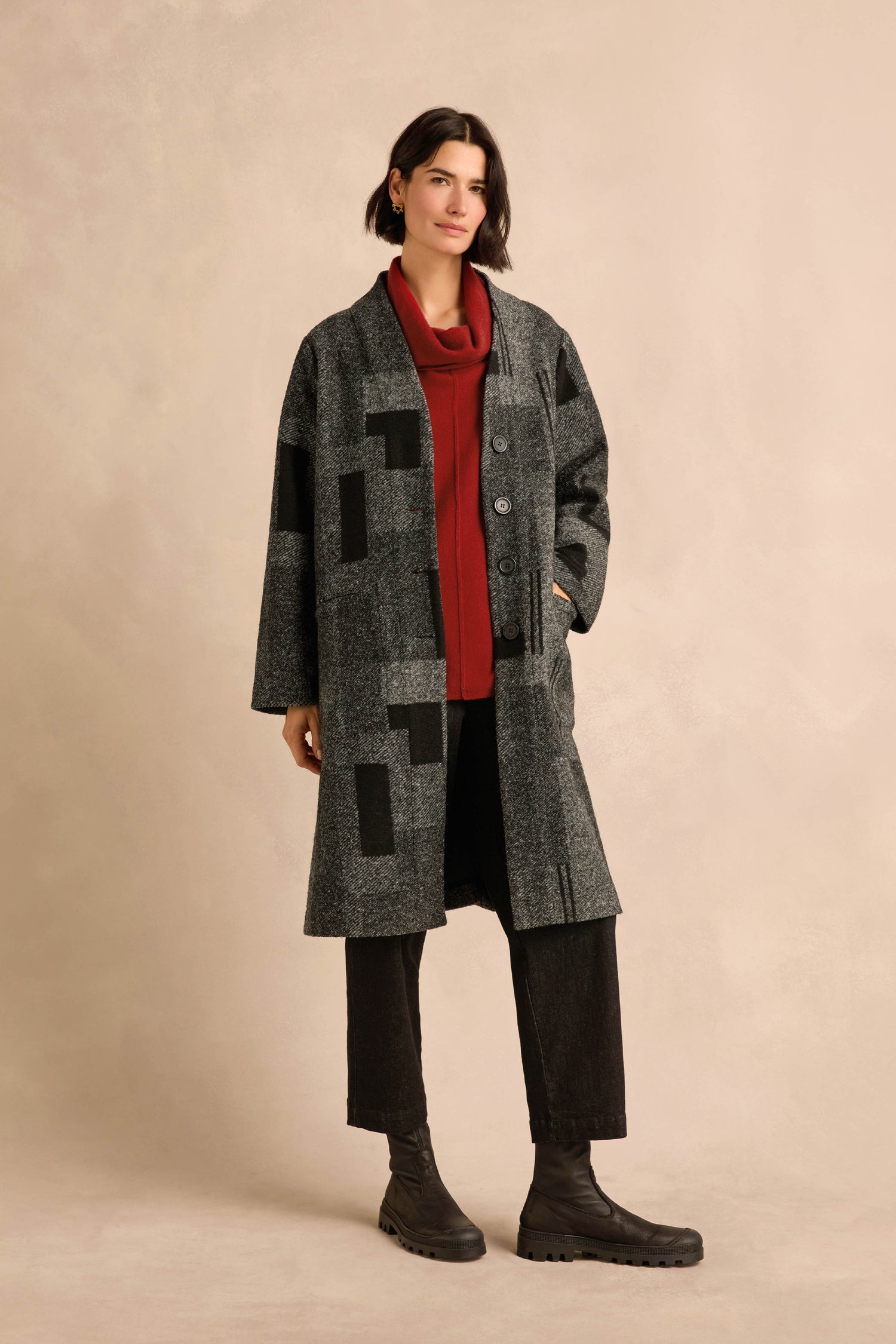 A person wearing the Melange Patchwork Wool Coat over a red top, paired with black pants and black boots, stands against a plain beige background.