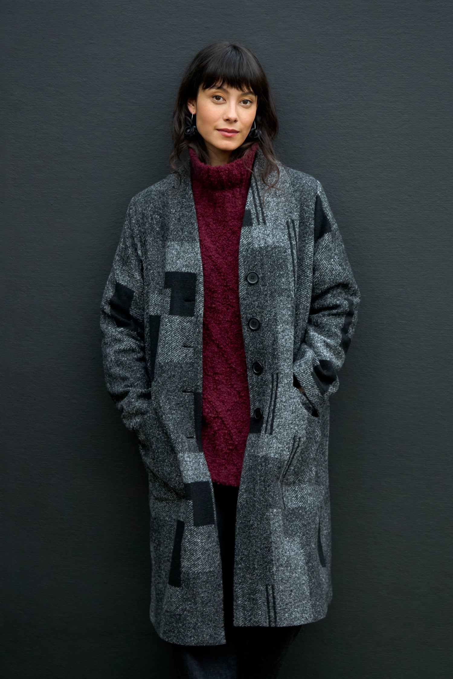 A woman wears a grey Melange Patchwork Wool longline coat over a dark red turtleneck sweater.