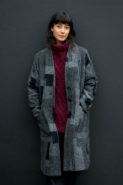 A woman wears a grey Melange Patchwork Wool longline coat over a dark red turtleneck sweater.