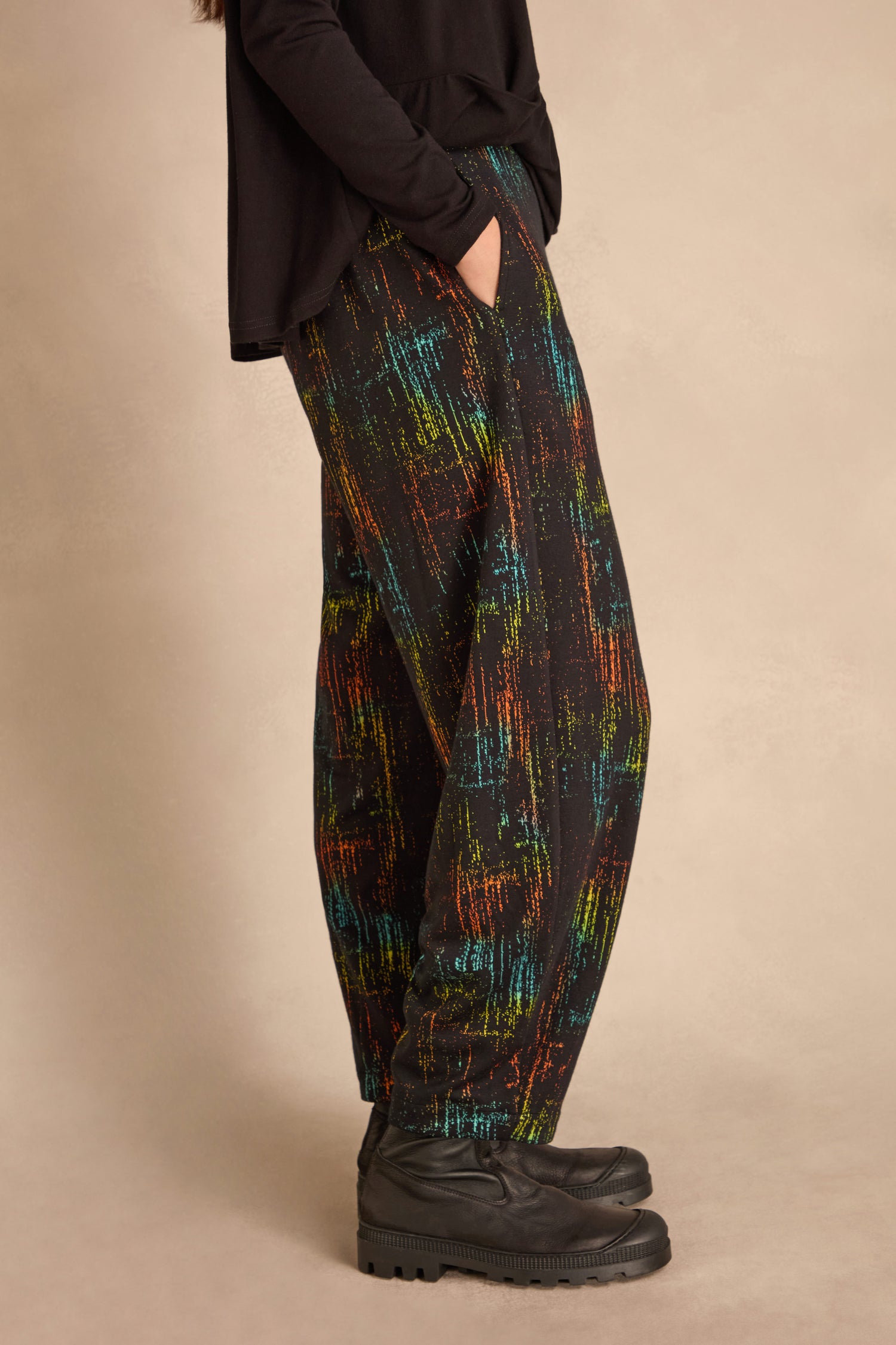 A person stands sideways with one hand in their pocket, wearing black shoes, a long-sleeve black top, and Space Dye Jacquard Bubble Trousers against a beige background.