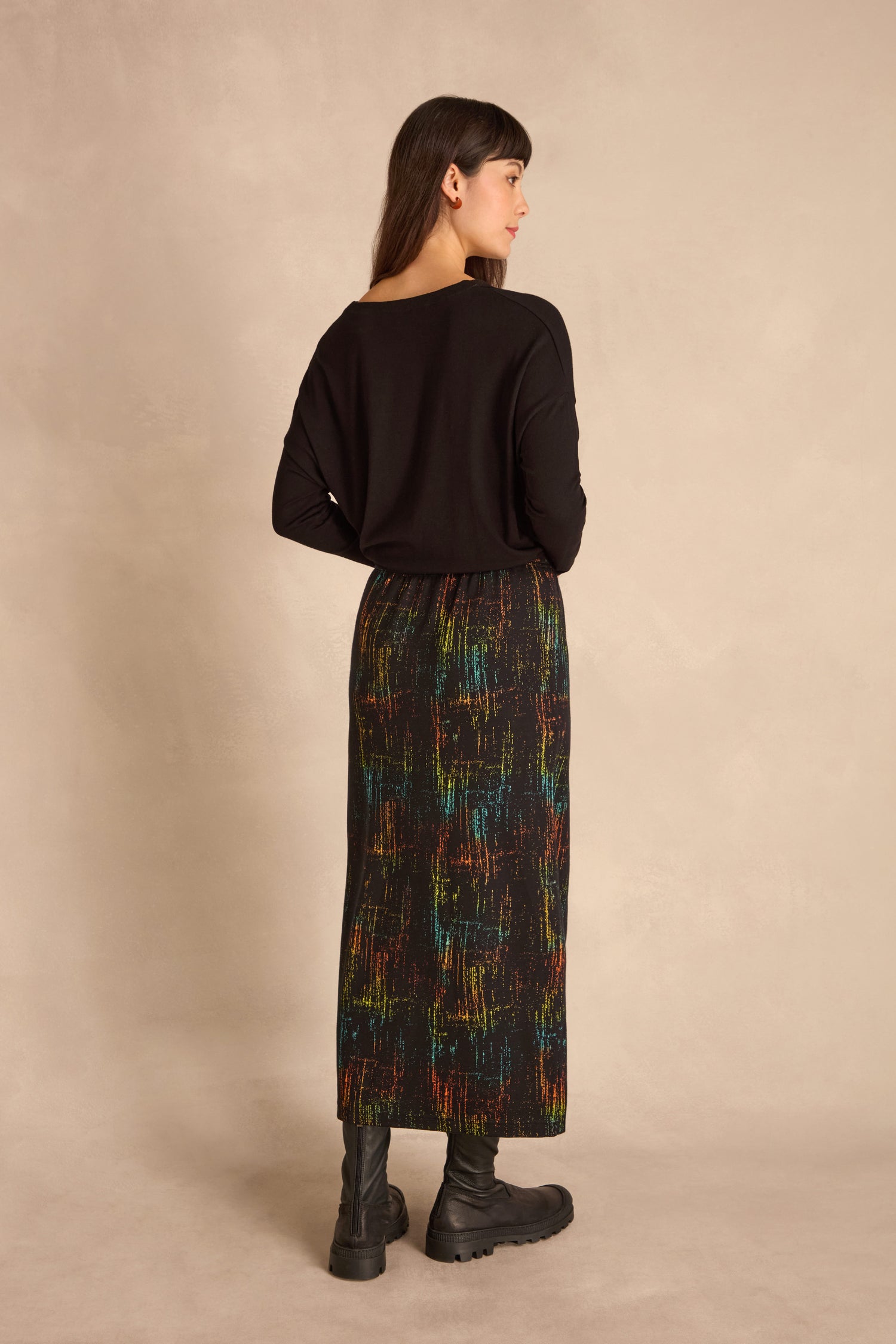 Woman standing with her back to the camera, wearing a black jacquard jersey top, Space Dye Jacquard Tube Skirt, and black boots against a neutral background.