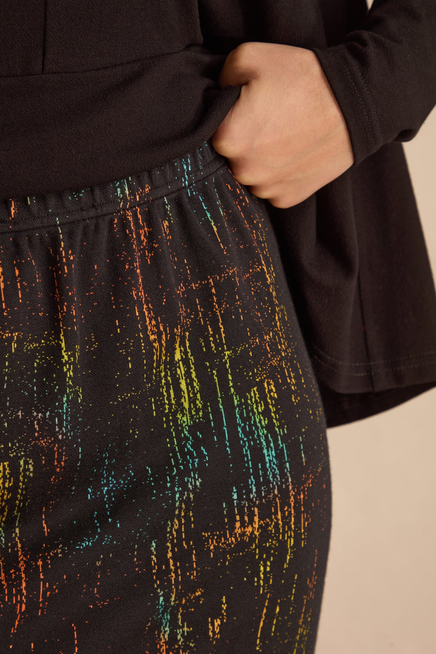 A person in a black top has their hand in the pocket of black abstract streak pants, paired with a Space Dye Jacquard Tube Skirt.