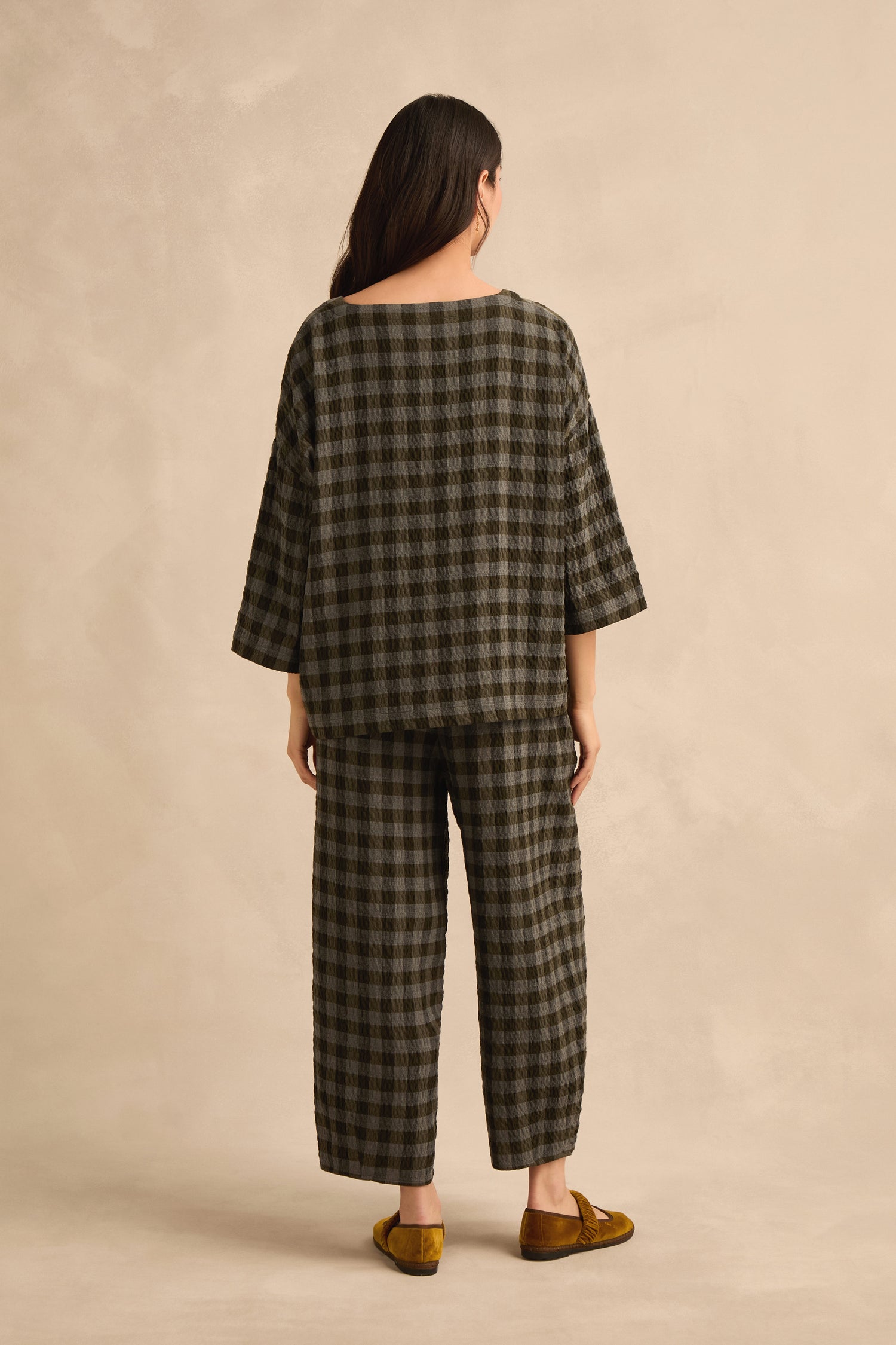 A person stands with their back to the camera, wearing the Crinkle Check Boxy Top in an oversized fit, paired with matching pants and yellow slip-on shoes against a neutral background.
