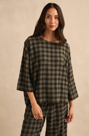 A woman stands against a beige background, facing forward with one hand by her side, wearing the Crinkle Check Boxy Top and matching pants in an oversized, loose fit.