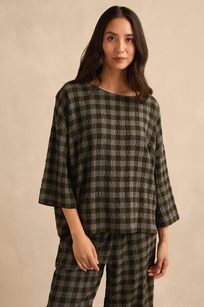 A woman stands against a beige background, facing forward with one hand by her side, wearing the Crinkle Check Boxy Top and matching pants in an oversized, loose fit.