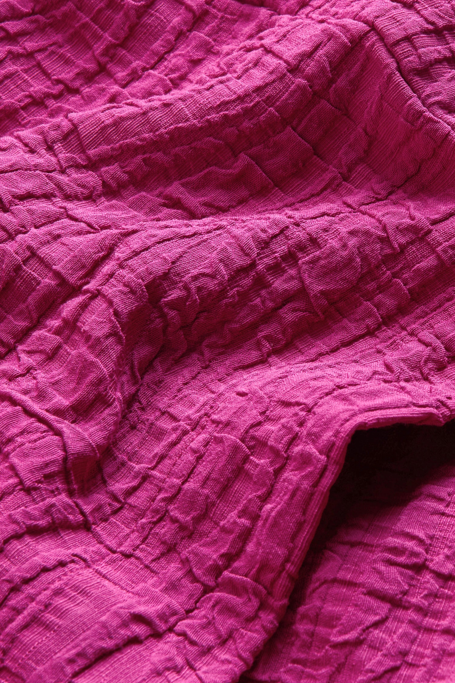 A close-up of the Magenta Wave Textured Crinkle Cowl Neck Top, highlighting its folded, crinkled magenta fabric with a distinct grid-like weave and deep shadows—ideal for showcasing the unique texture and relaxed boxy silhouette of this statement piece.