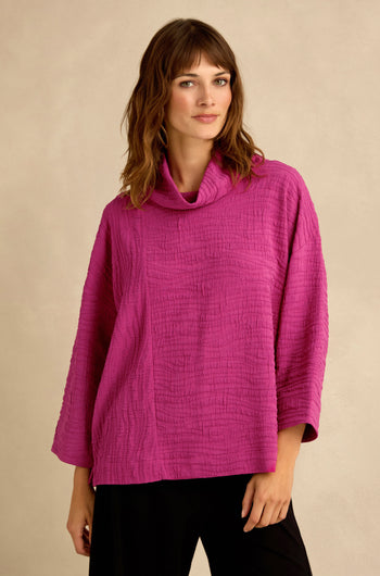 A woman wearing the Magenta Wave Textured Crinkle Cowl Neck Top, featuring a wave crinkle fabric, three-quarter sleeves, and a relaxed boxy silhouette, stands against a plain beige background.