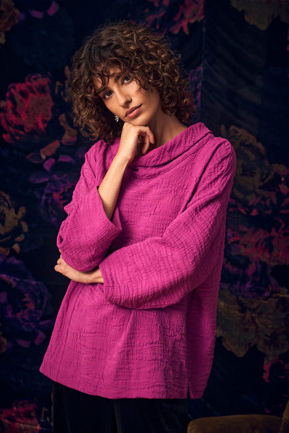 A person wears a Magenta Wave Textured Crinkle Cowl Neck Top, featuring a magenta, wave-textured, long-sleeve design with a relaxed cowl neck.
