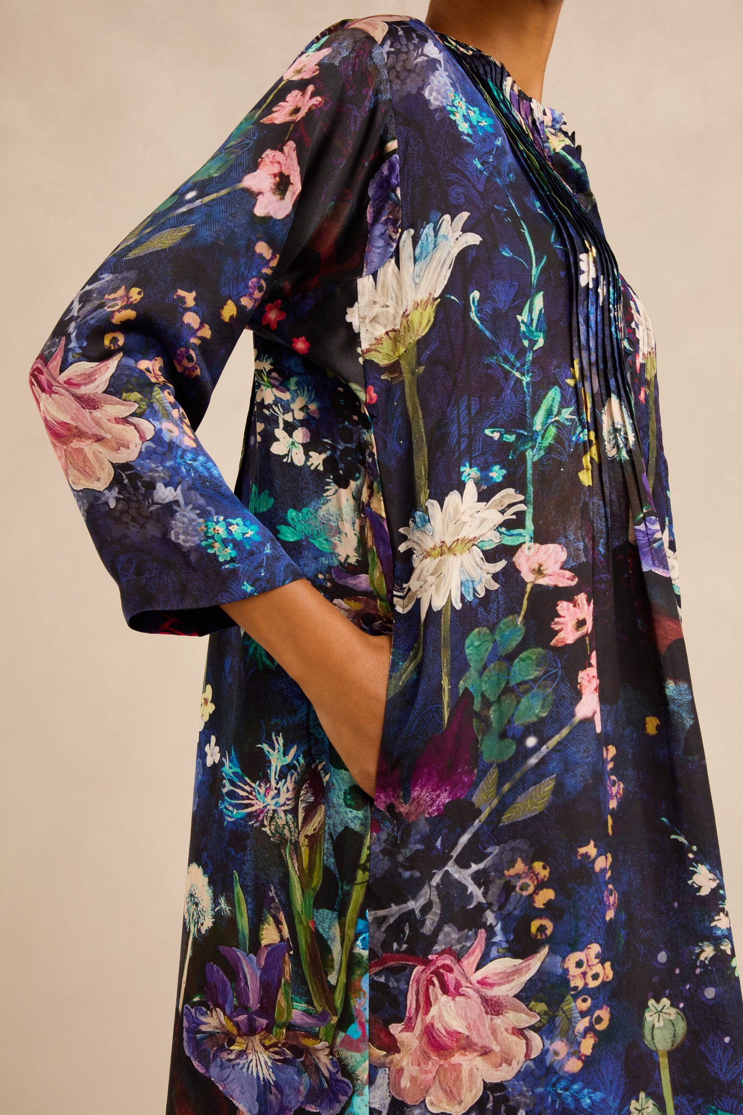 Wearing the Floral Bouquet Pleated Dress, which features long sleeves, a dark blue background with a vibrant floral print, and convenient side pockets.