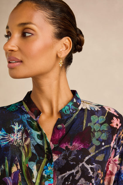 A woman with her hair in a bun wears the Floral Bouquet Flared Shirt and gold drop earrings, gazing to the side against a neutral background.