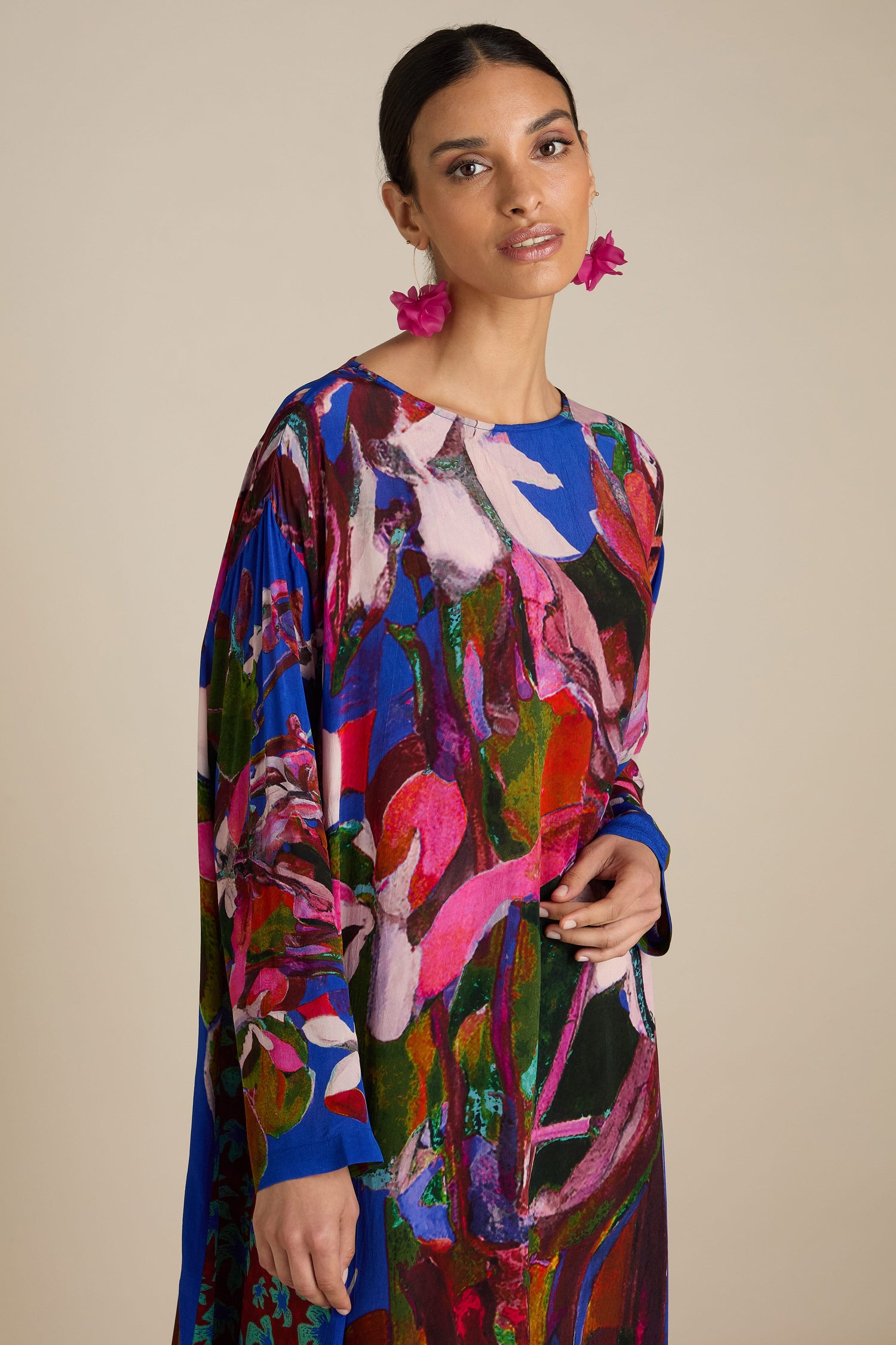 A woman wearing a Side Panel Flower Print Dress with pink flower earrings stands against a plain background, flaunting the relaxed free-flowing silhouette and bold abstract florals of her Side Panel Flower Print Dress.