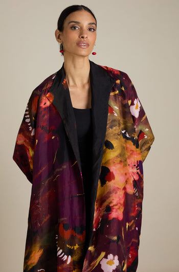 A woman with dark hair pulled back wears a Reversible Abstract Flower Print Jacket over a black top, exuding artful elegance against a light neutral background.