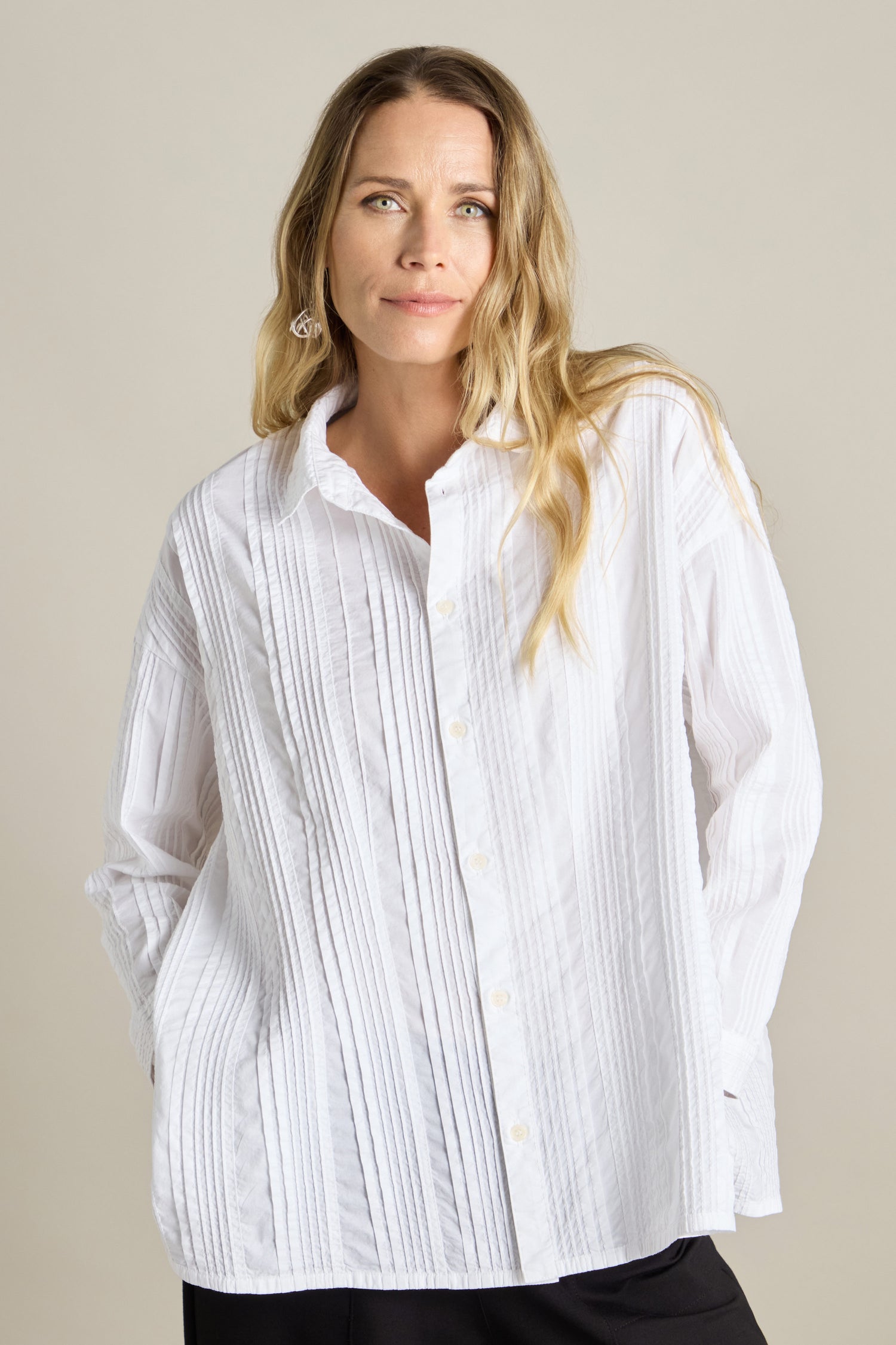 A person with long, light brown hair wearing a white, oversized fit Multi Pleat Shirt by Yacco Maricard from YaccoMaricard.