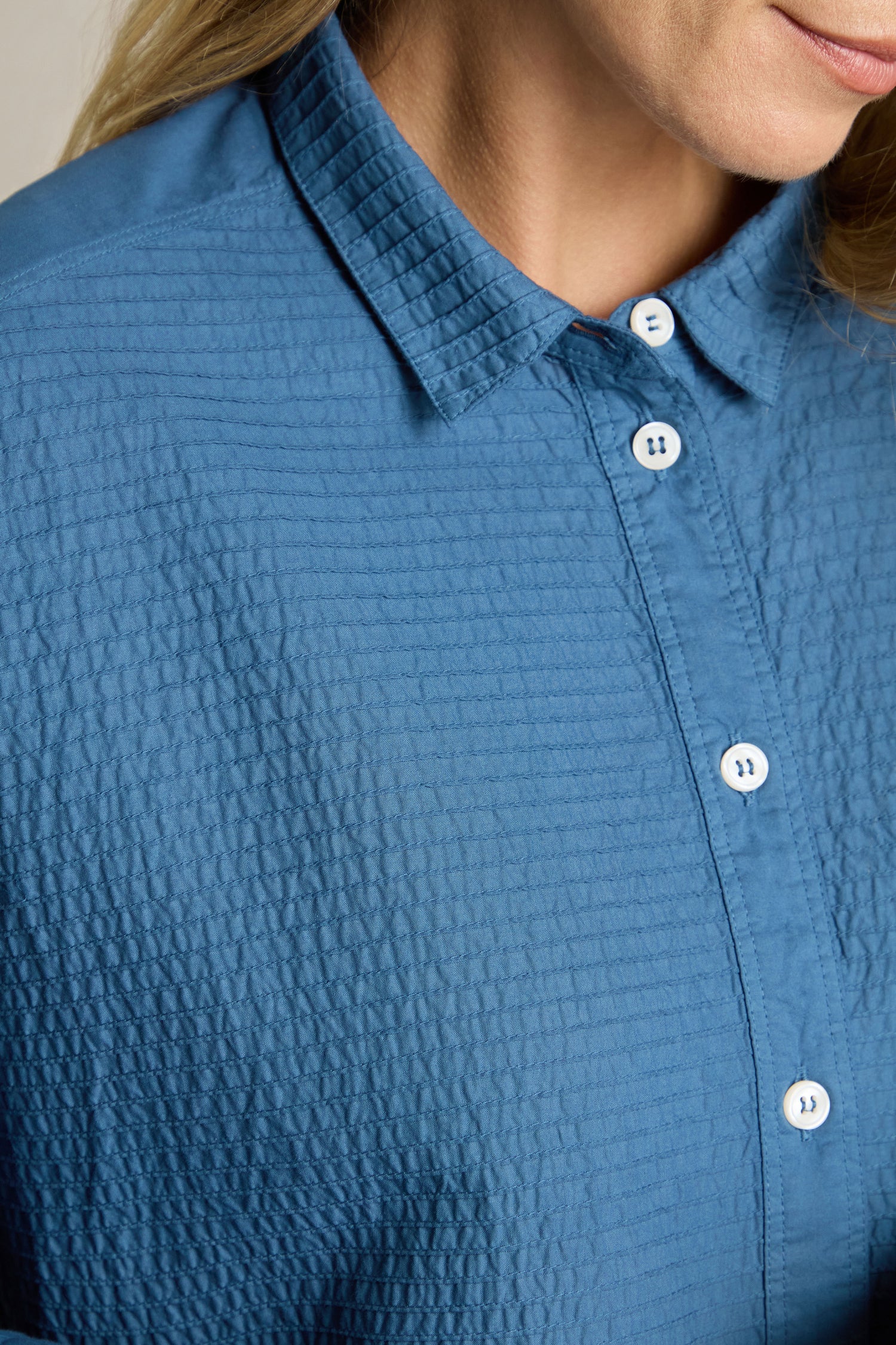 A person is dressed in a Deep Hem Pleated Shirt from Yacco Maricard, showcasing its textured blue fabric. Only their lower face, shoulder, and chest areas are visible—exuding a modern classic vibe.