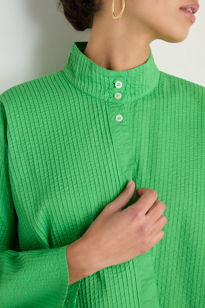 A person wearing the Asymmetric Cotton Bright Green Shirt, featuring a stand neck, Japanese textile-inspired texture, and three white buttons, holds the shirt near their chest.