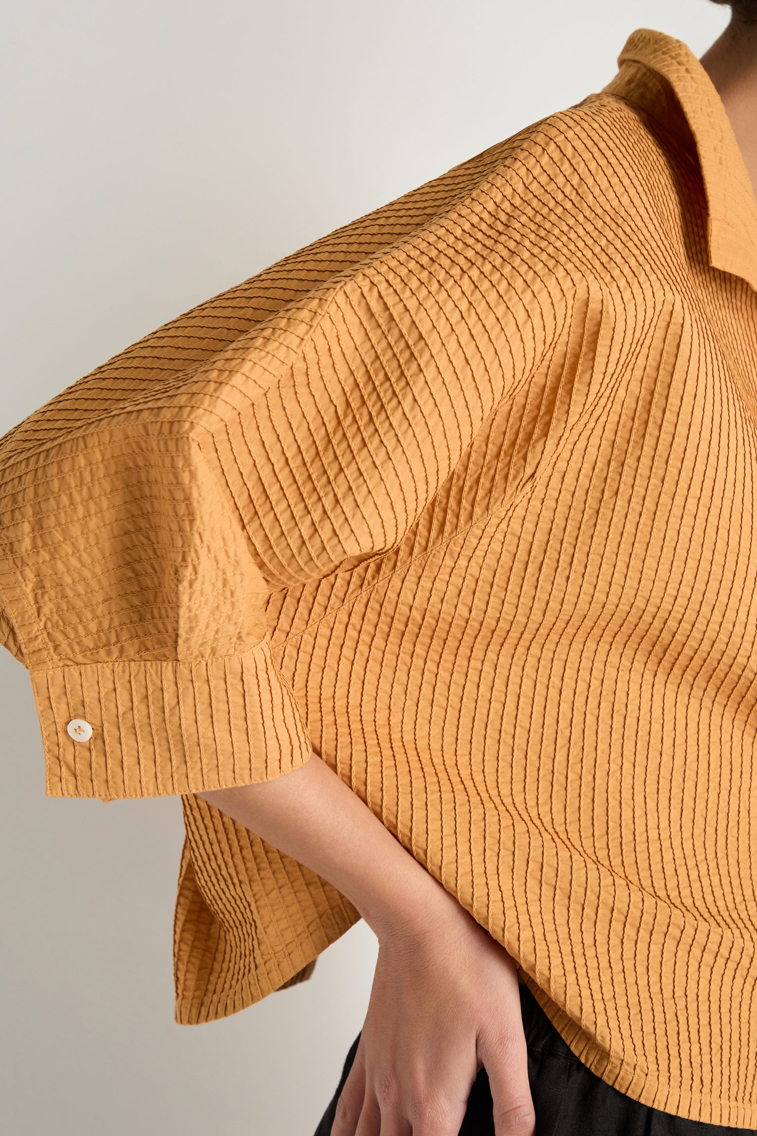 A person wears the Pleated Sleeve Brown Shirt, featuring a loose fit, textured fabric, pleated sleeves, a collar, and a boxy silhouette. They are shown from the side with one arm bent.