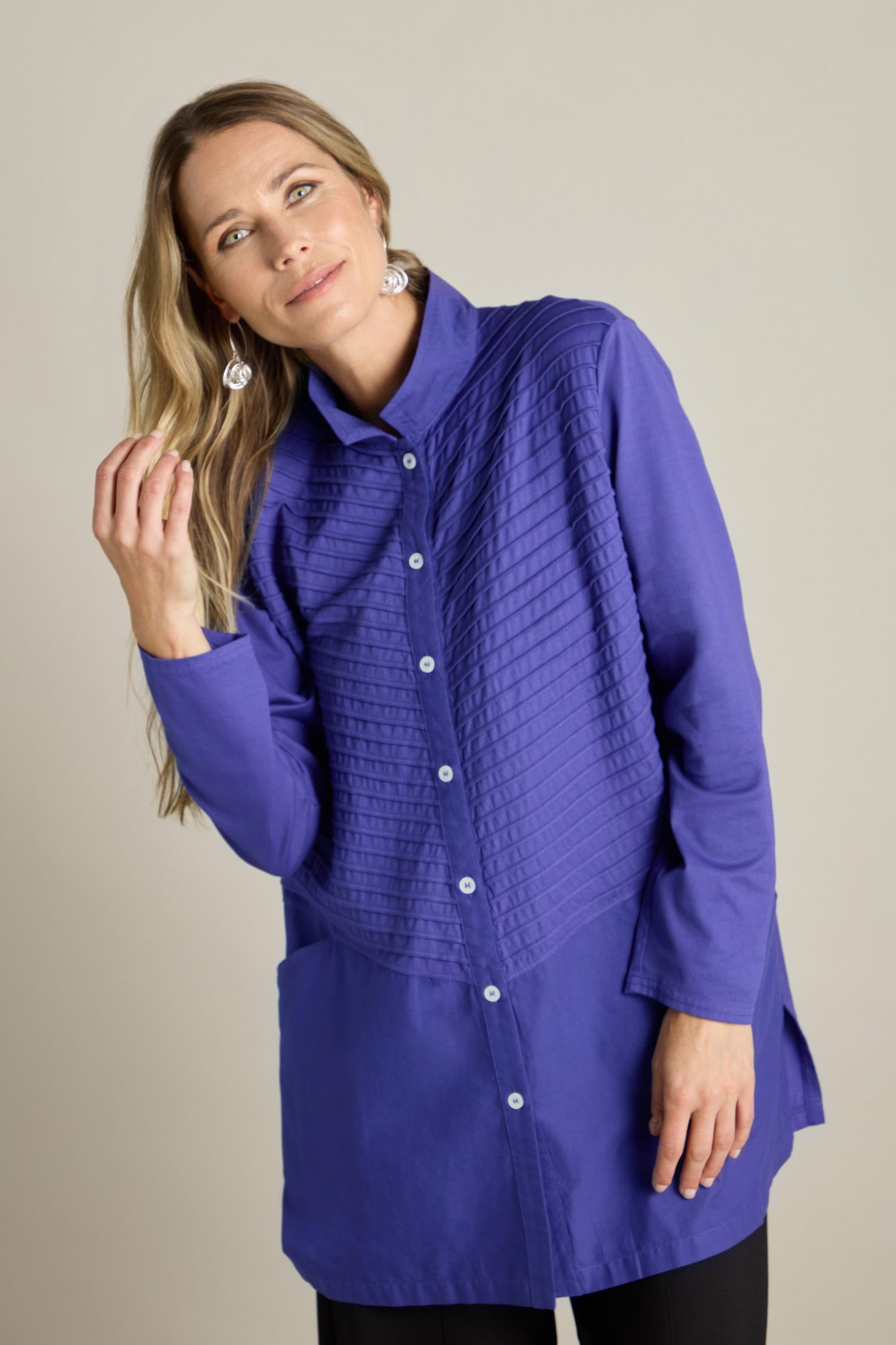 A woman with long blonde hair in a Cotton Jersey And Calico Overshirt featuring an embroidered placket smiles slightly while touching her hair.