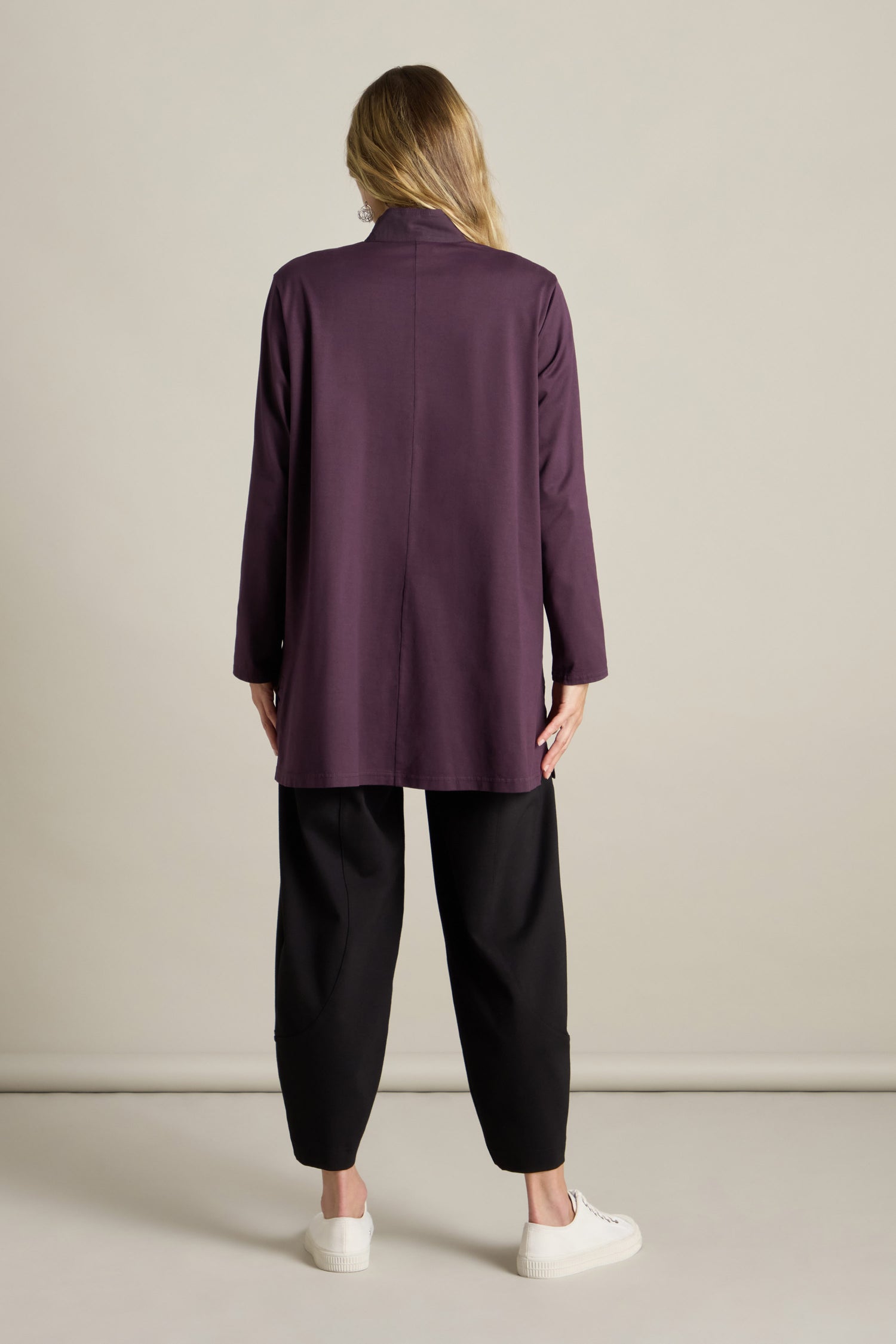 A person stands facing away, exuding style in a deep purple Cotton Jersey and Calico Overshirt paired with black pants and white sneakers, the ensemble strikingly enhanced by an embroidered placket.