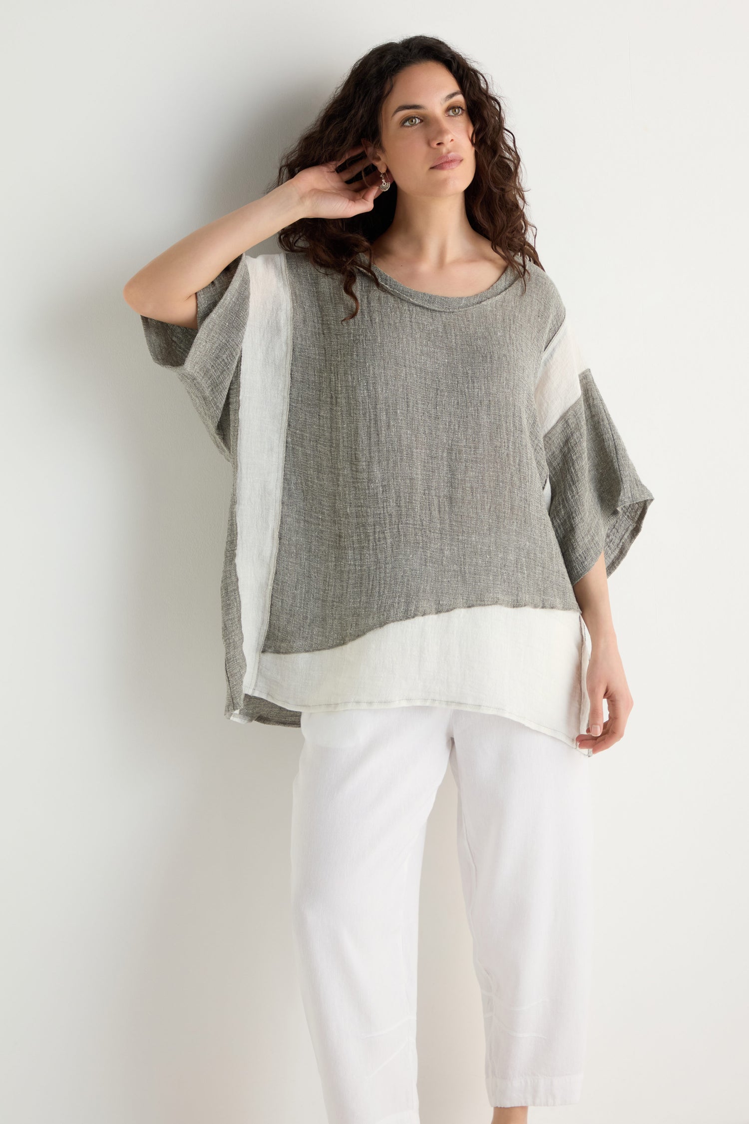 A person wears a loose, short-sleeved Linen Blend Boxy Tunic in gray and white with contrast panels, paired with white pants, standing against a plain white background.