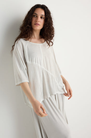 A woman with long curly hair wears a relaxed fit Seam Detail Jersey Top and matching pants in light-colored viscose jersey, featuring asymmetric seams, standing against a white backdrop.