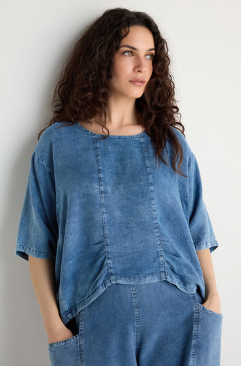 A woman with long curly hair, hands in her pockets, stands against a plain white wall wearing the Lyocell Panelled Boxy Top and matching pants.