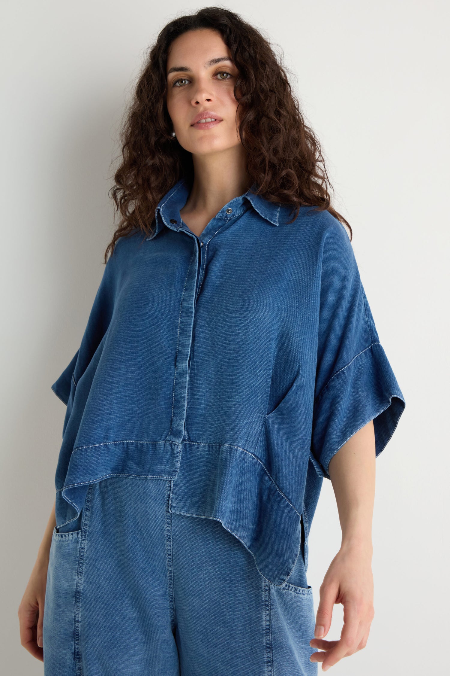 Woman with curly hair wearing the Lyocell Boxy Shirt and matching denim pants, standing against a plain light-colored background.