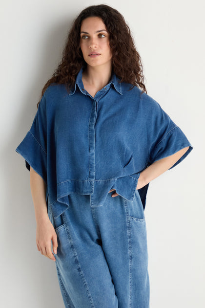 Woman with long curly hair wearing a Lyocell Boxy Shirt and high-waisted denim jeans, standing against a plain white background.