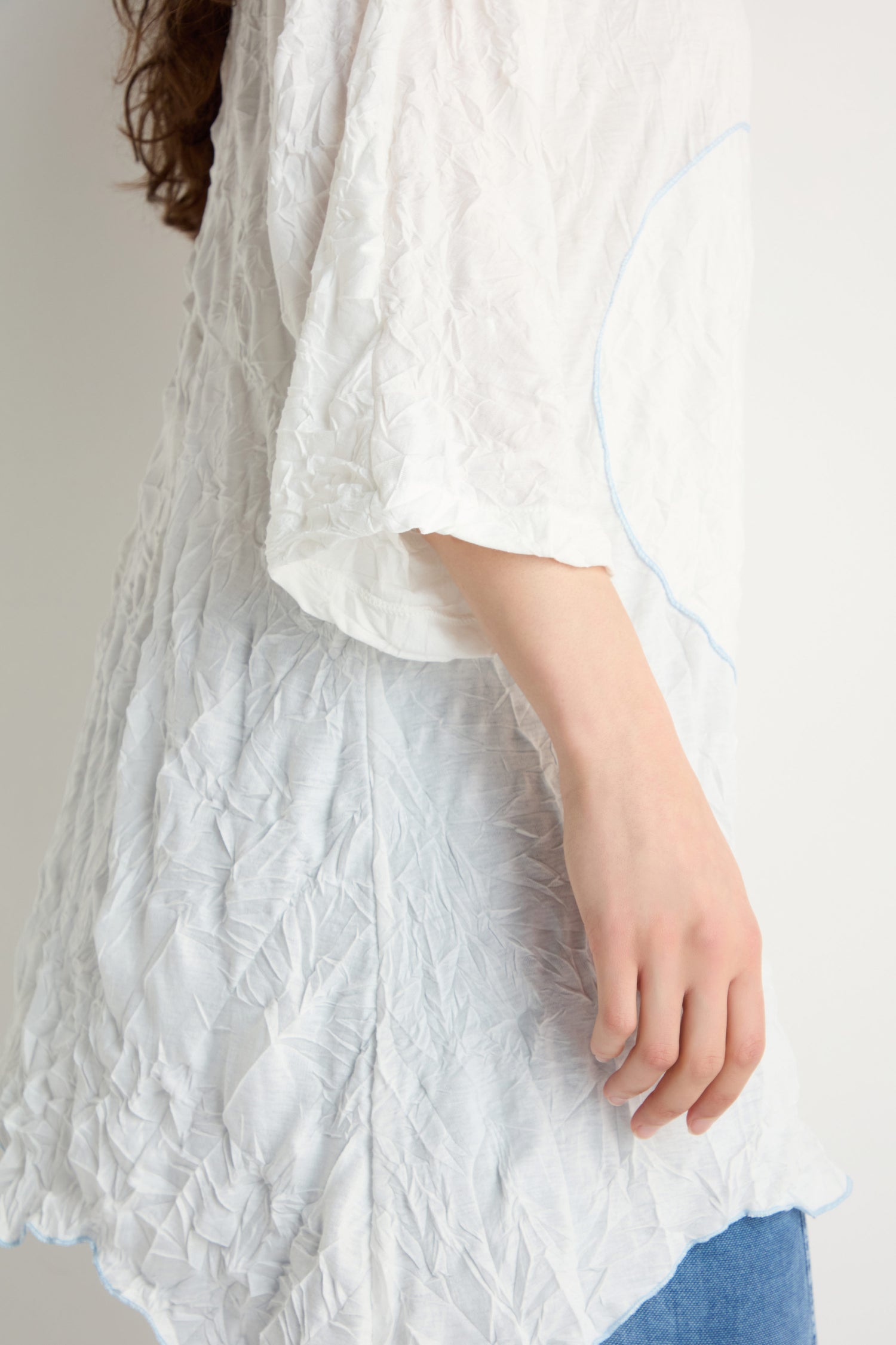 A person is shown from the torso up, standing sideways against a plain background, wearing the Embroidered Circles Crinkle Tunic in white with loose sleeves and blue jeans.
