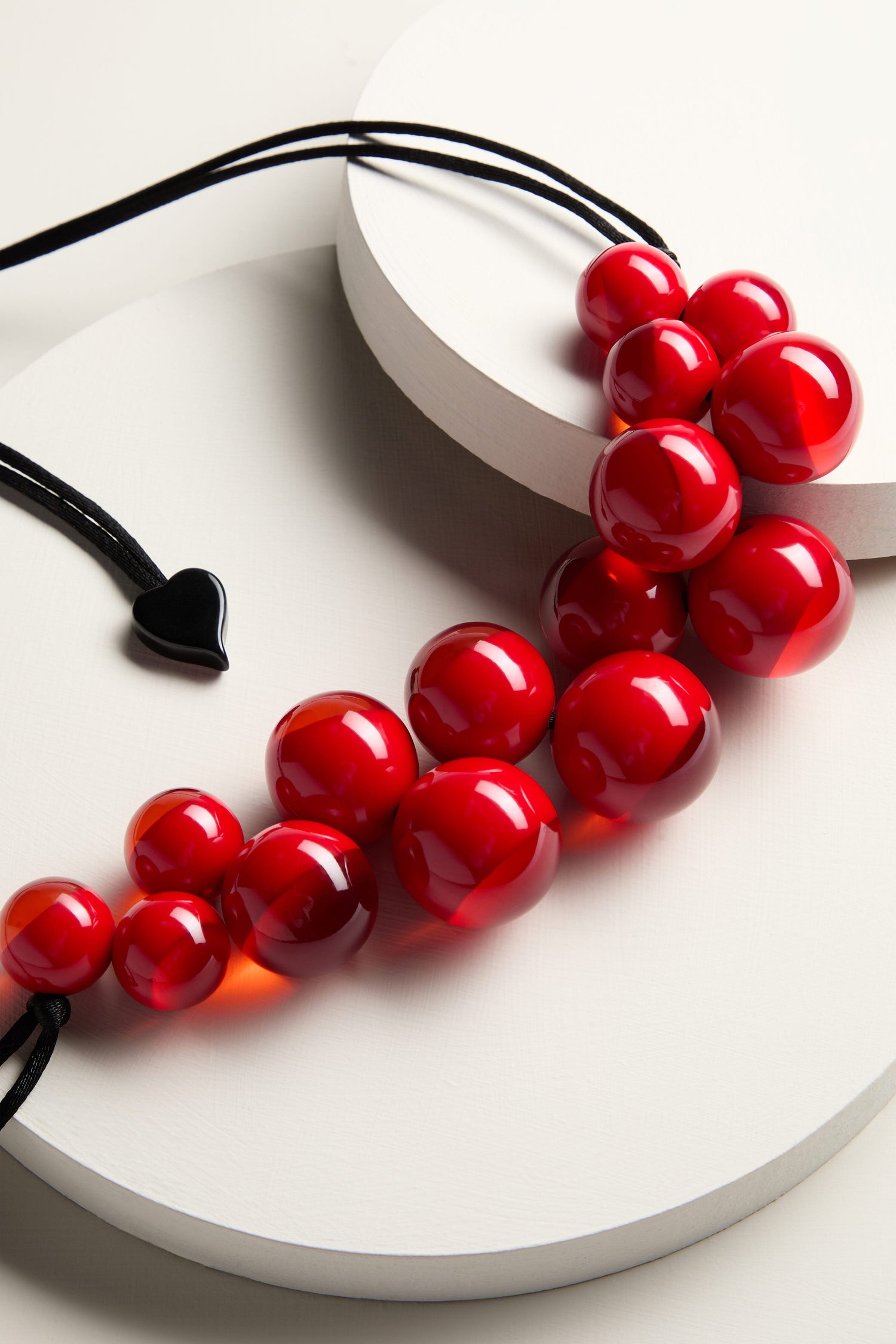 A handmade Spheres Necklace featuring a red bead design resting on a white surface.