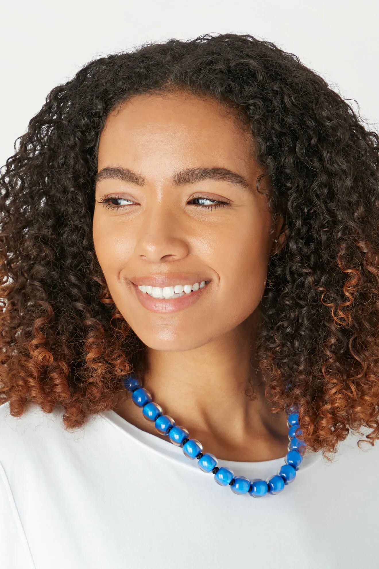 A quirky woman wearing a Colourful Bead Necklace with curly hair.