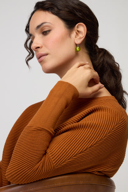 Woman with wavy brown hair in a ponytail, wearing a rust-colored ribbed sweater and Colourful Bead Resin Earrings, seated in profile with her hand near her neck.