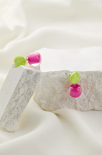 Colourful Beads Double Sphere Earrings featuring green and pink high-quality resin beads, displayed on white textured stone slabs with a cream-colored fabric background.