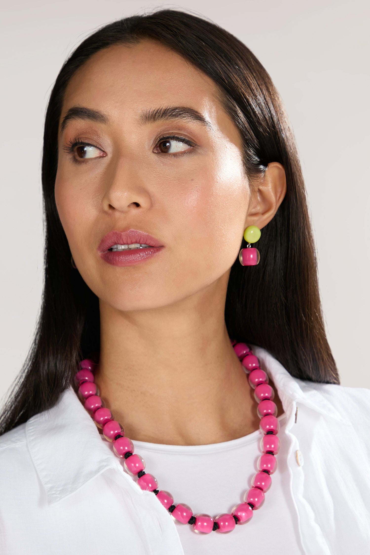 A woman with long, straight hair wears a white blouse, a vibrant pink beaded necklace of high-quality resin beads, and matching Colourful Beads Double Sphere Earrings. She looks slightly to the side.