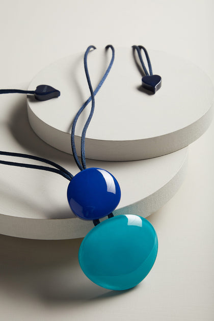 A Resin Sphere Pendant necklace with blue and black beads on a white surface.