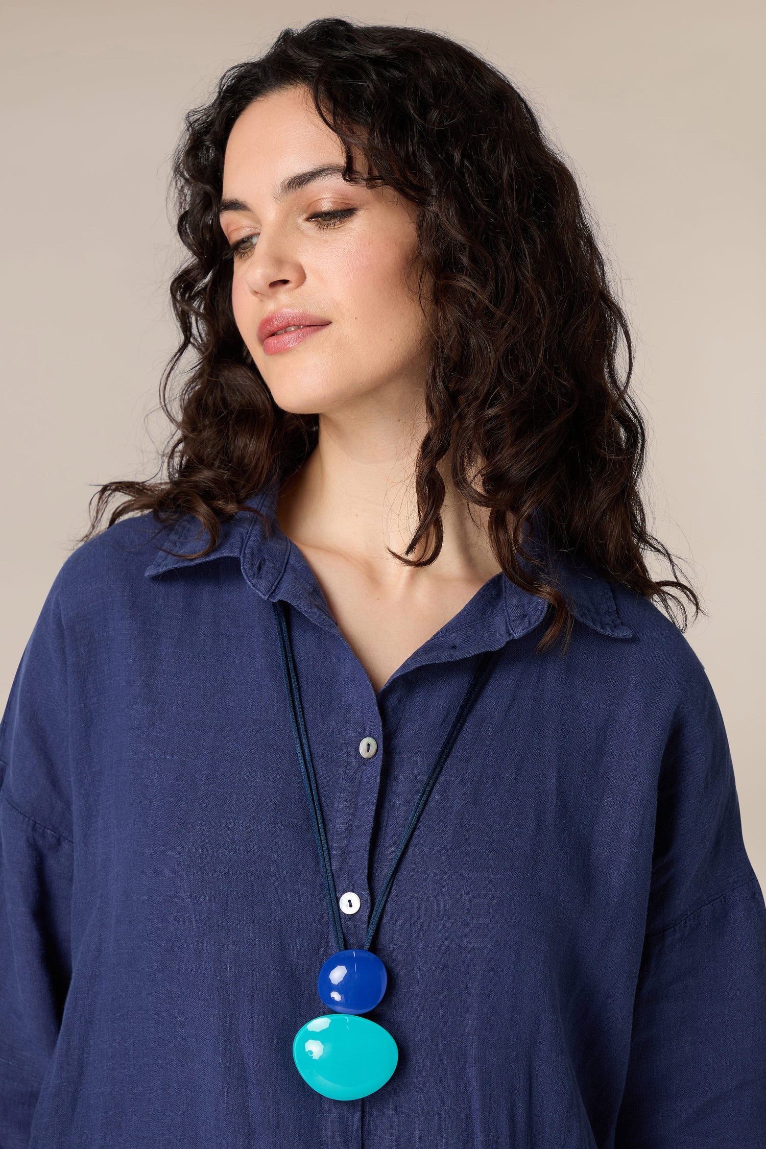 A woman with long curly hair wearing a blue shirt accessorized with a Resin Sphere Pendant.