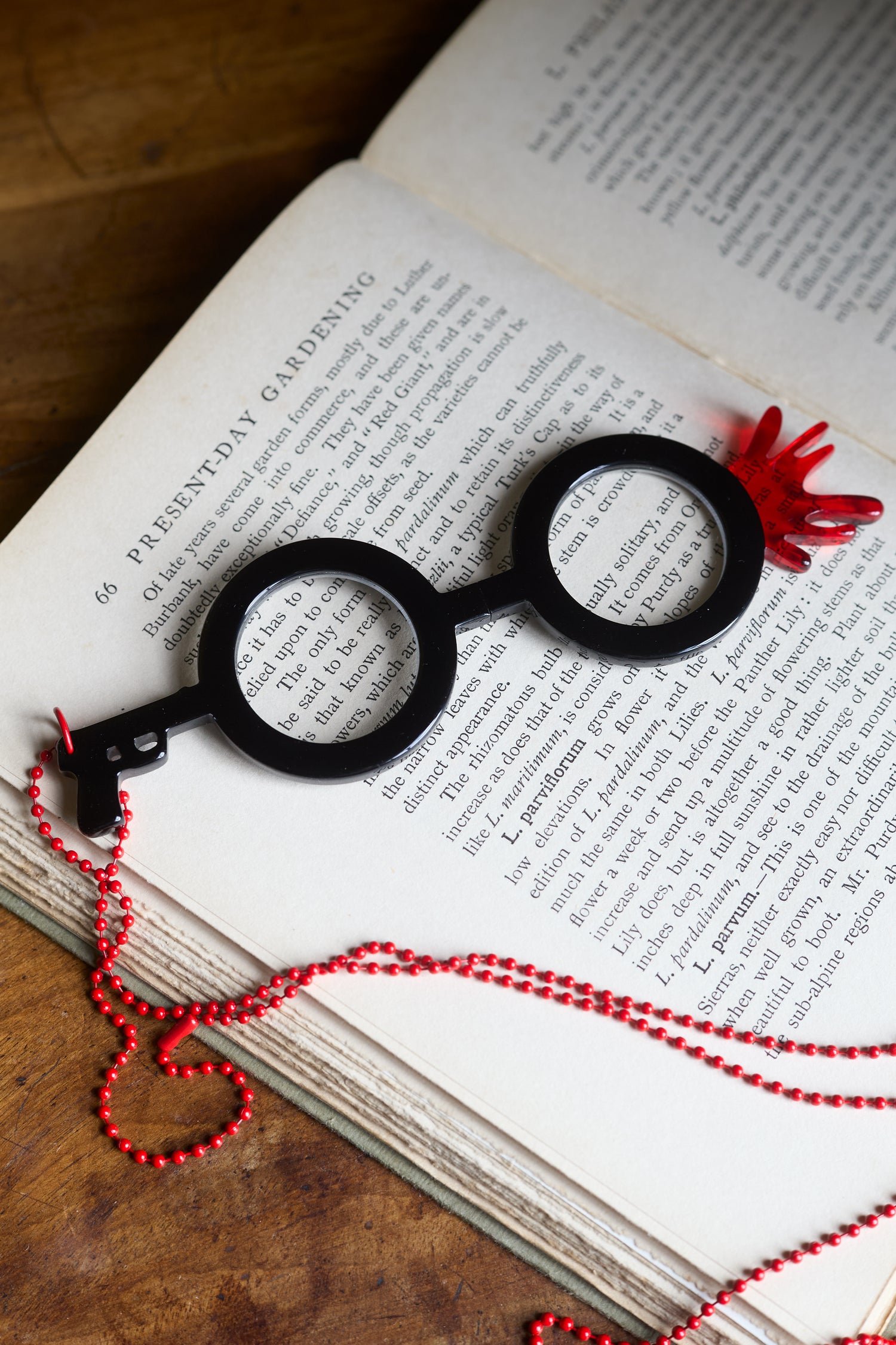 A pair of Revolver Pendant Glasses with black frames and red accents sits atop the open pages of a gardening book.