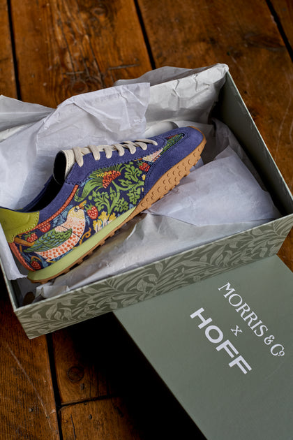 The Blue William Morris Bridge Trainers, featuring the iconic Strawberry Thief print, are displayed in an open shoebox on a wooden surface, highlighting these stylish sneakers for women.