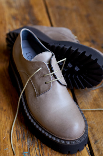 A pair of Two Tone Lace Up Leather Brogues with thick black soles, crafted from beige and black leather, placed on a wooden floor.