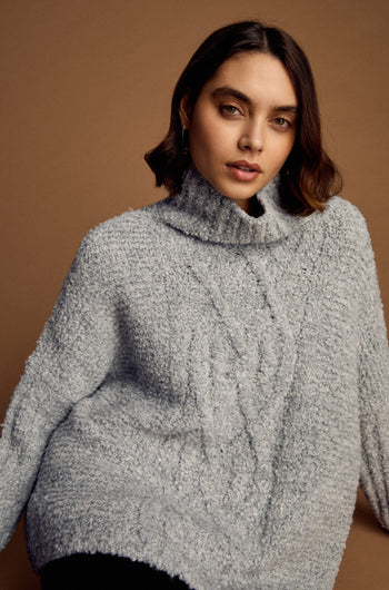 A woman with short brown hair wears the Boucle Cable Knit Jumper, posing against a plain brown background.