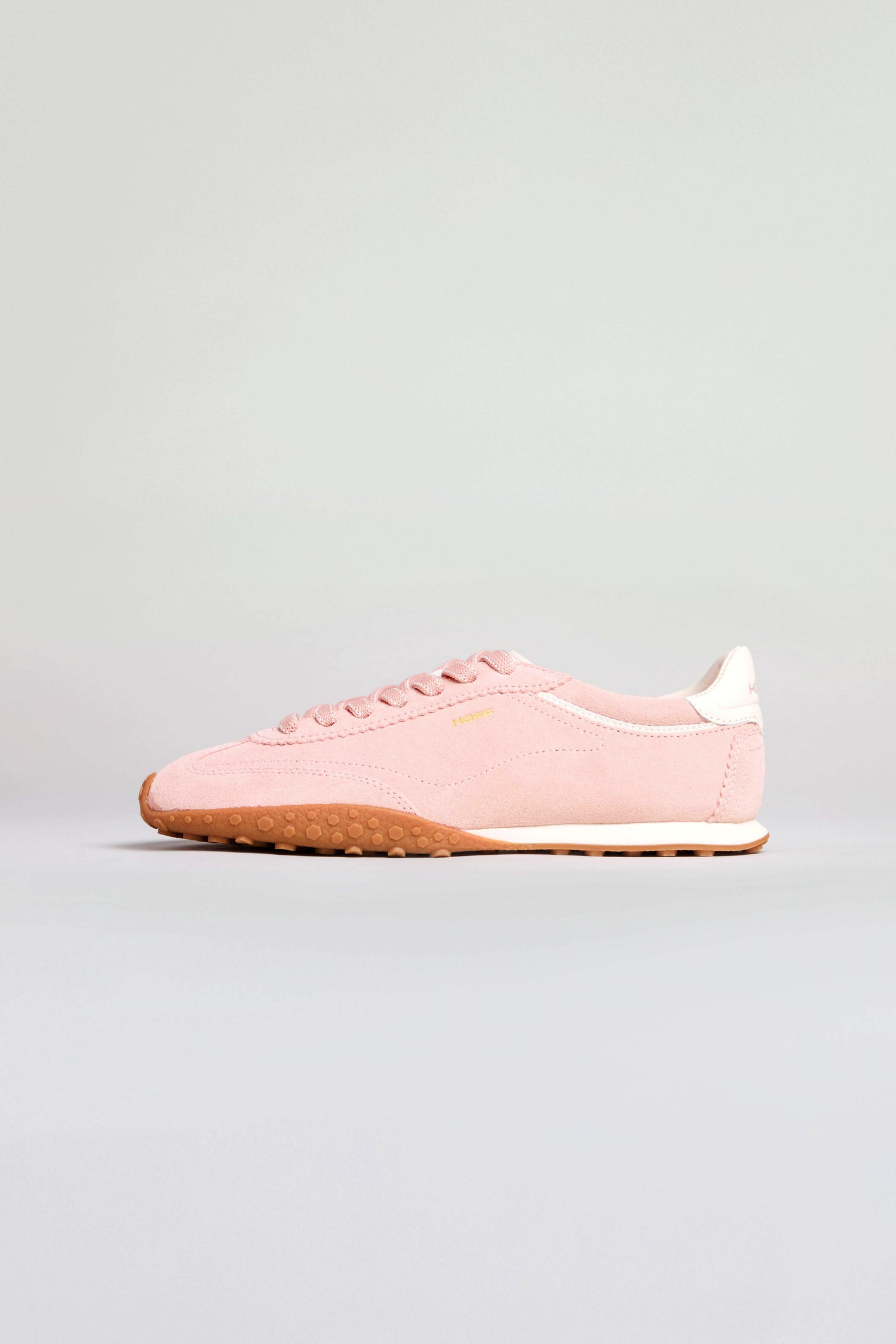 A single Bridge Rose Suede Trainer in pink with a tan rubber sole and white heel detail is displayed against a plain light backdrop, offering a subtle retro running vibe.