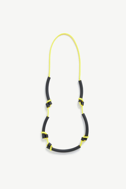 The Twists Necklace by Samuel Coraux is a unique accessory featuring black cylindrical beads connected by vibrant yellow strings, forming an eye-catching loop.