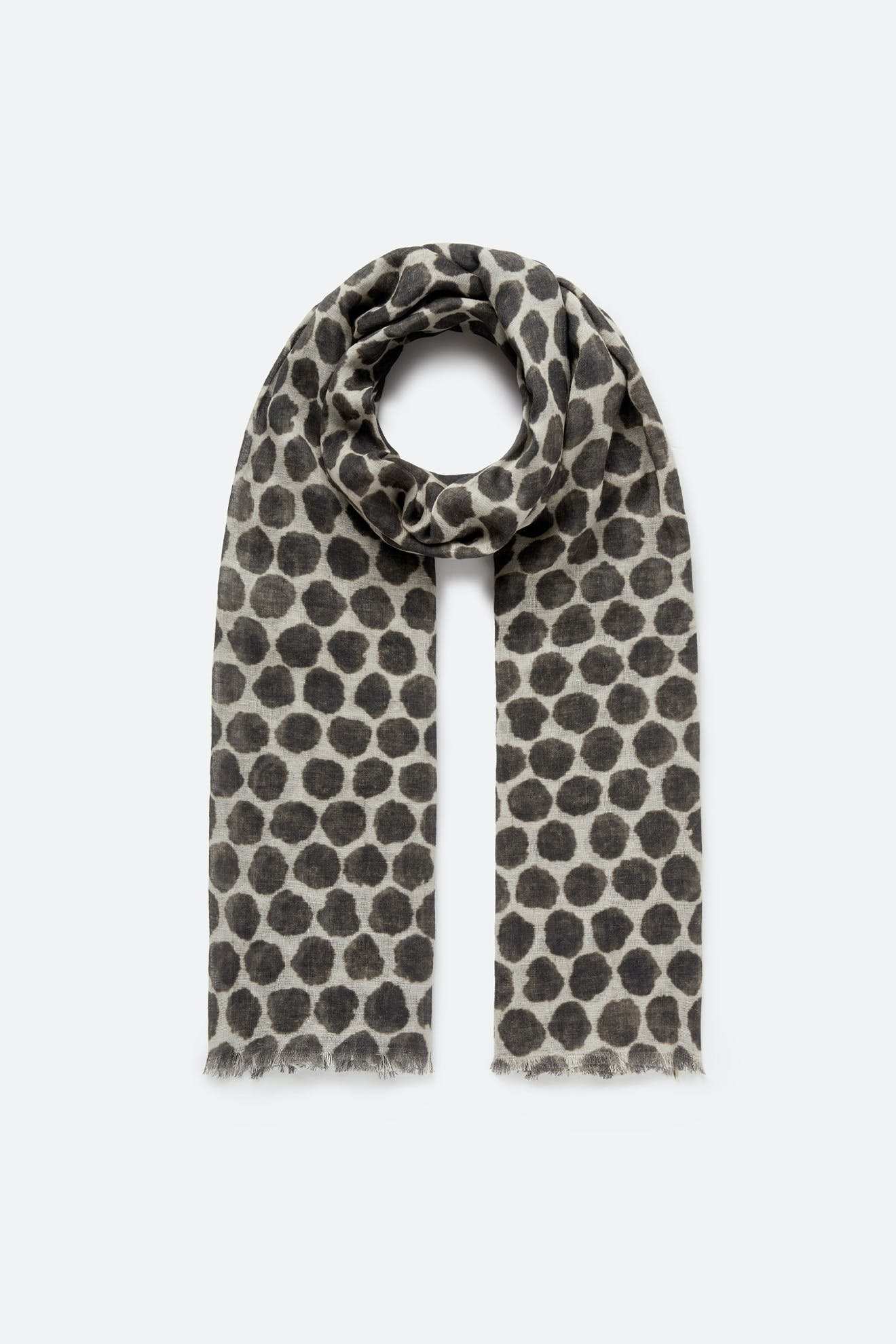 The Circle Spot Scarf is a gray, lightweight accessory featuring a black polka dot pattern. Loosely rolled with frayed edges and photographed on a plain light background, this cotton modal linen scarf brings effortless style and comfort to any look.