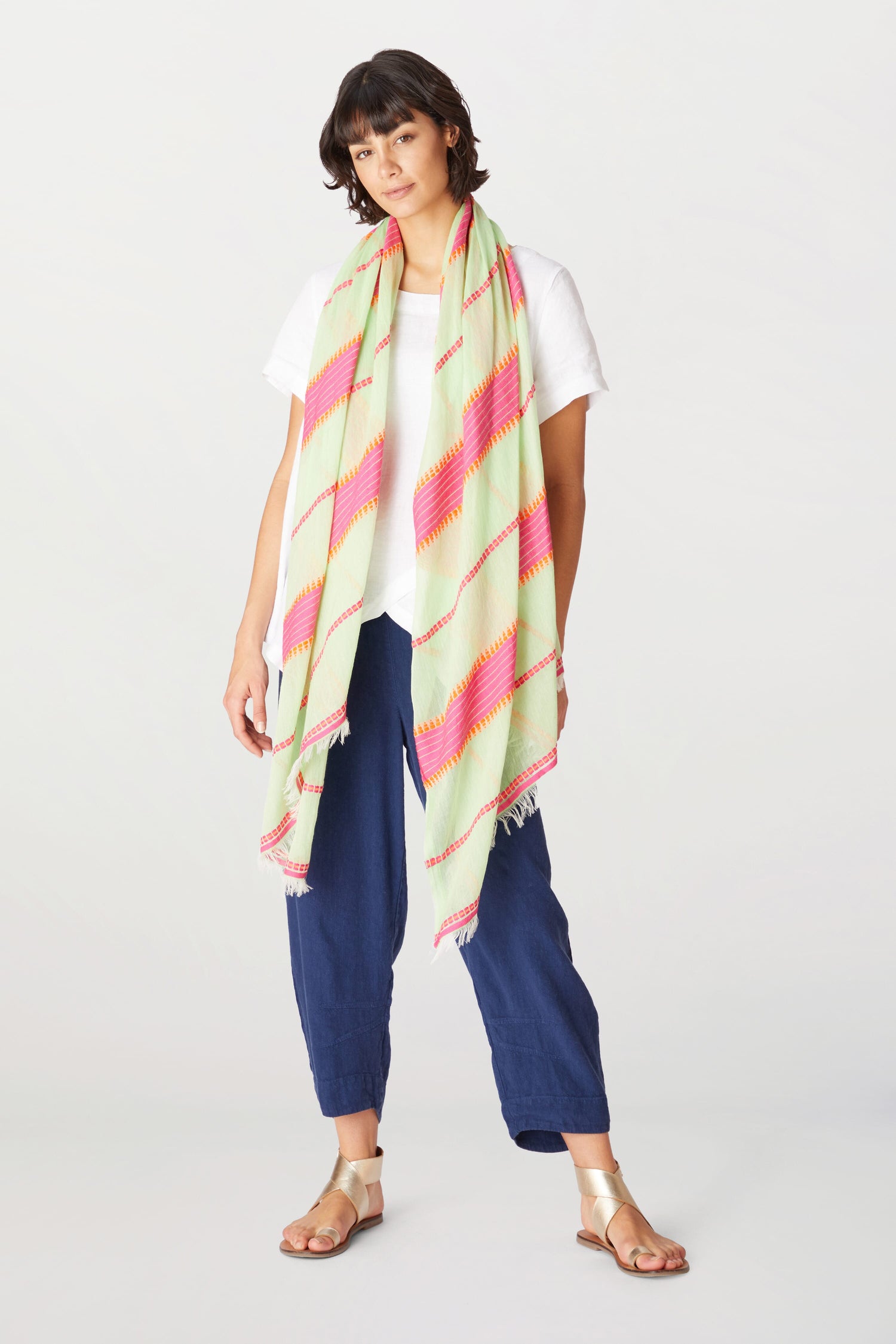 A woman in a white t-shirt, navy trousers, and sandals stands with a Colorful Peacock Feather Silk Scarf draped over her shoulders.